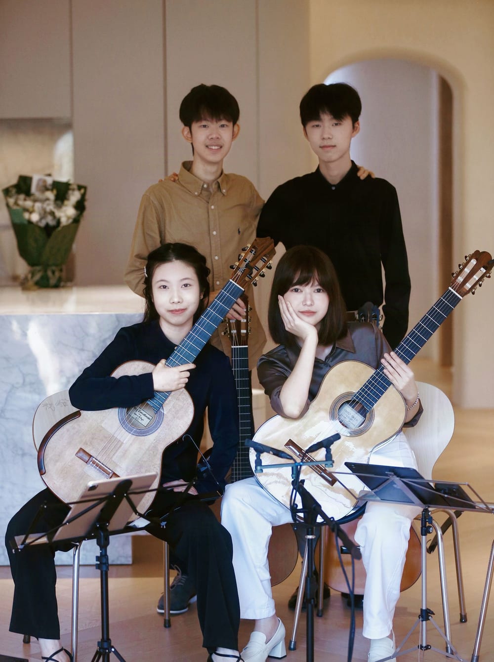 The four players of Primal Guitar Quartet together: two sit in front holding their guitars, two stand behind, and iPads rest on the music stands before them.